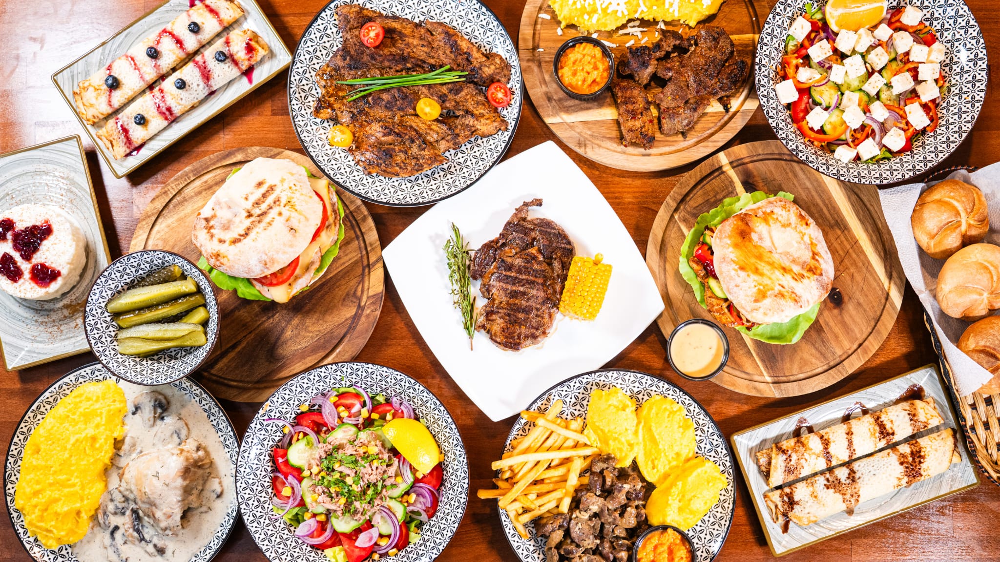 Masă cu preparate românești văzută de sus, la un restaurant tradițional din Galați: fripturi, mămăligă cu ciulama, salate, burgeri și deserturi